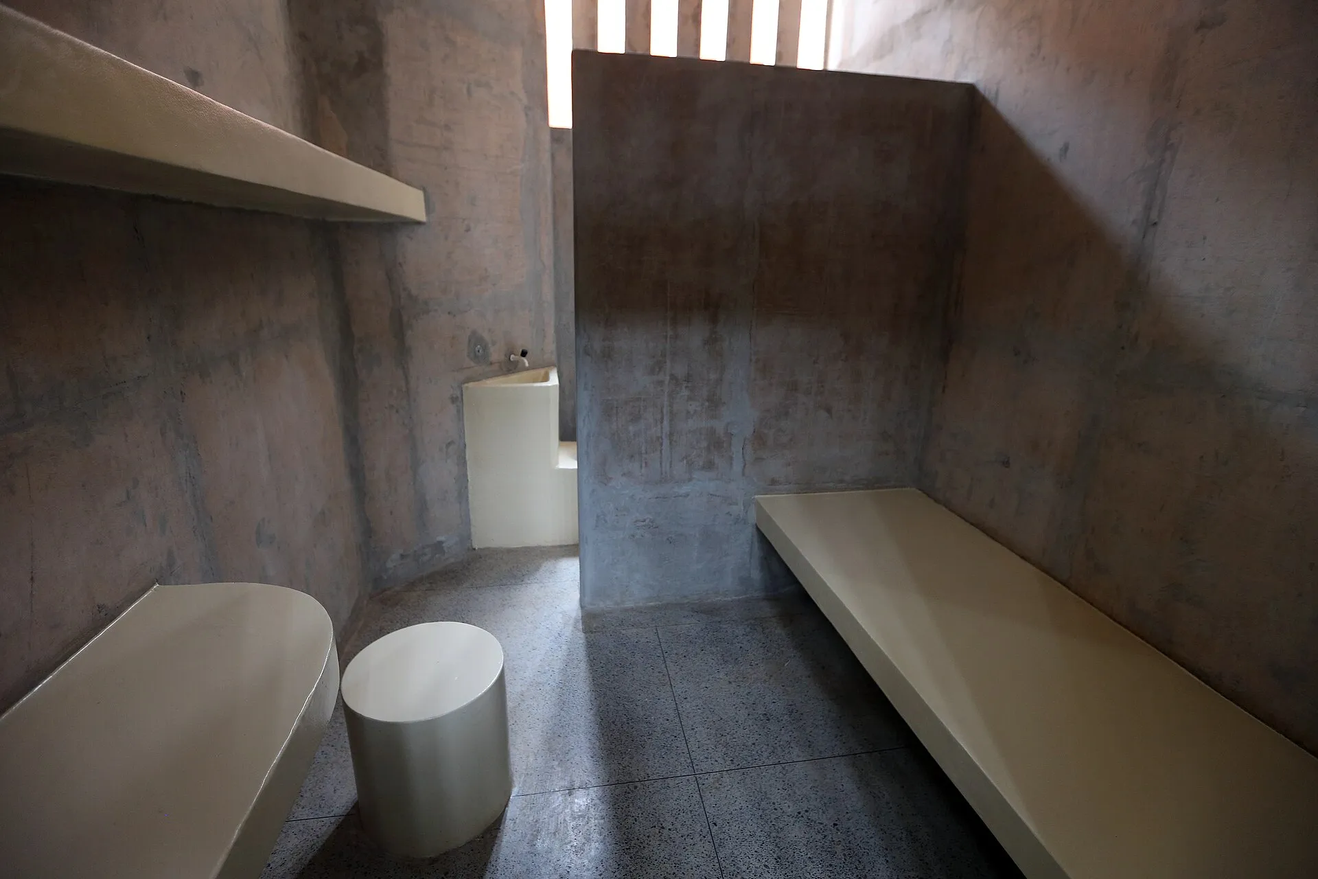 Cela de concreto com bancos e uma pia, com janela estreita e gradeada no alto, na penitenciária federal de Brasília.