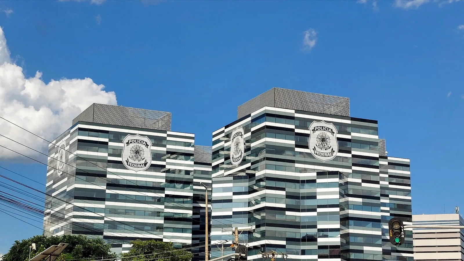 Prédio espelhado da nova sede da Polícia Federal em Brasília, com o brasão da instituição nas fachadas, sob céu azul.