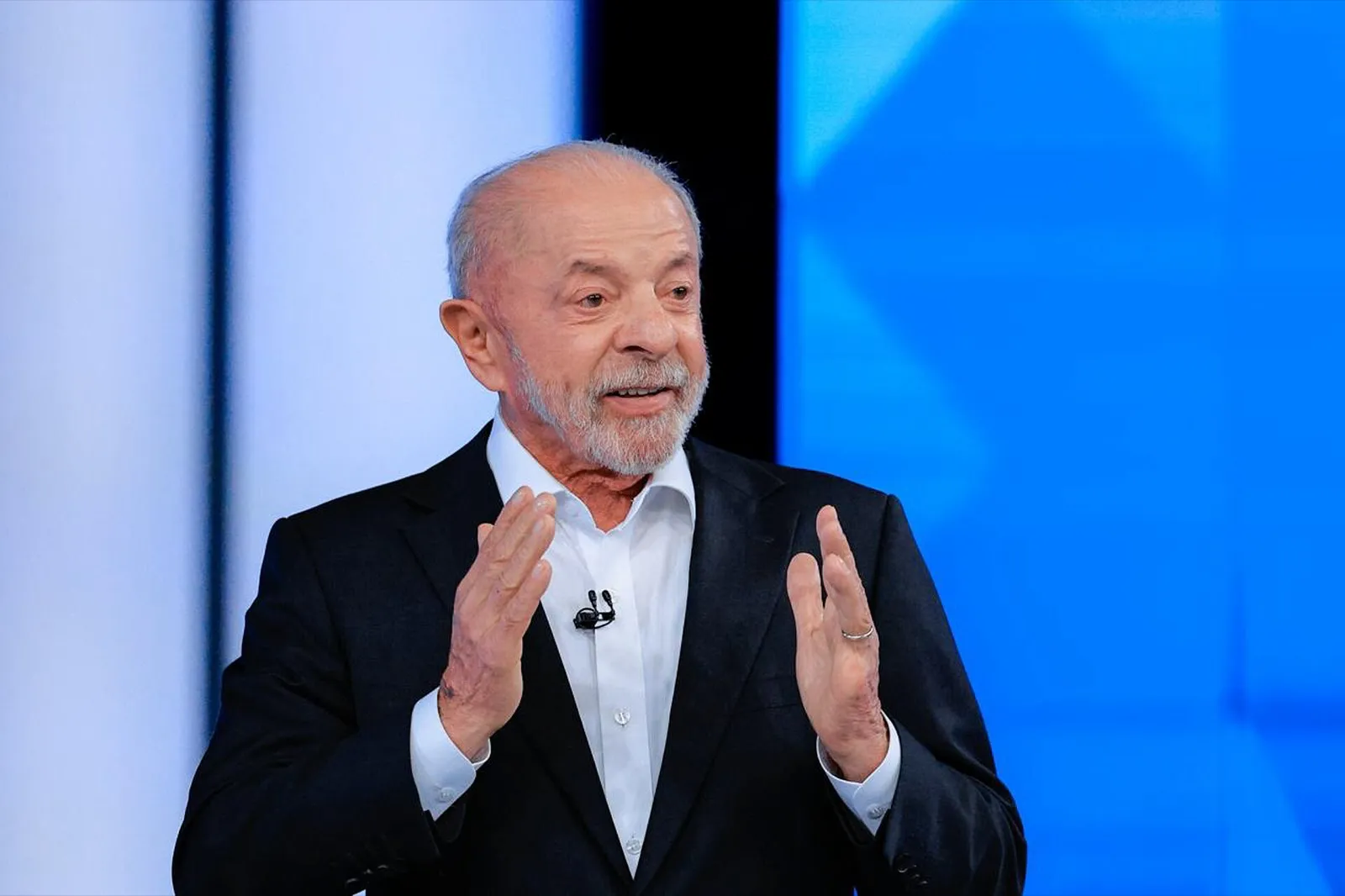 Lula, de terno escuro e microfone de lapela, gesticula diante de um cenário azul de TV, durante o debate da Globo.