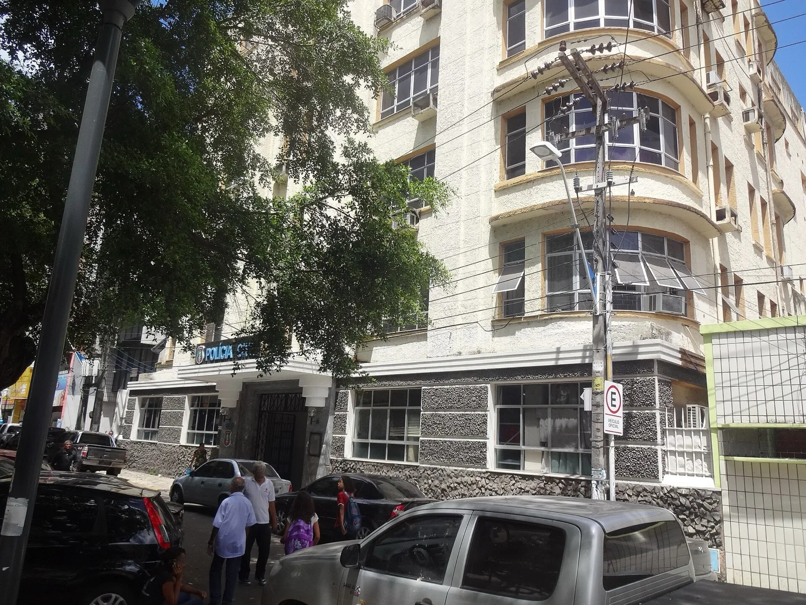 Fachada de prédio de cinco andares em estilo art déco, com a placa da Polícia Civil na entrada, em rua de Fortaleza com carros estacionados e pedestres.