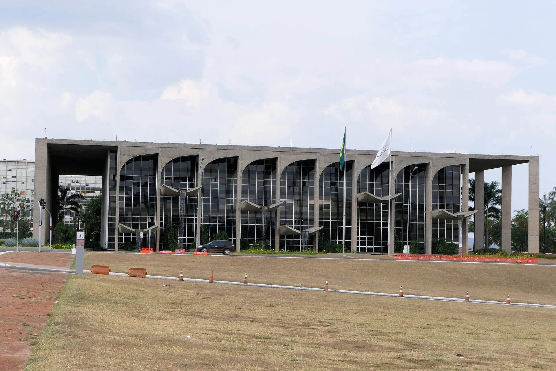 Fachada de concreto e vidro do Palácio da Justiça, em Brasília, com grandes arcos e colunas, bandeira do Brasil e céu nublado.
