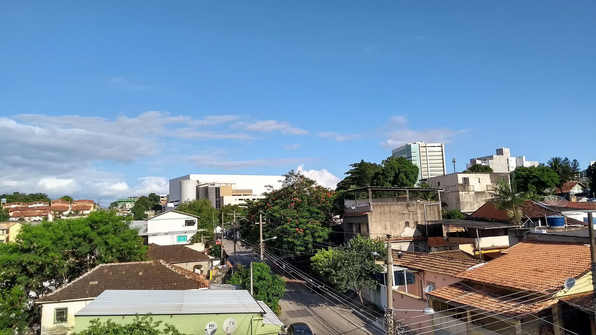 Vista elevada de casas, prédios e ruas do bairro Chacrinha, em Nova Iguaçu, sob céu azul.