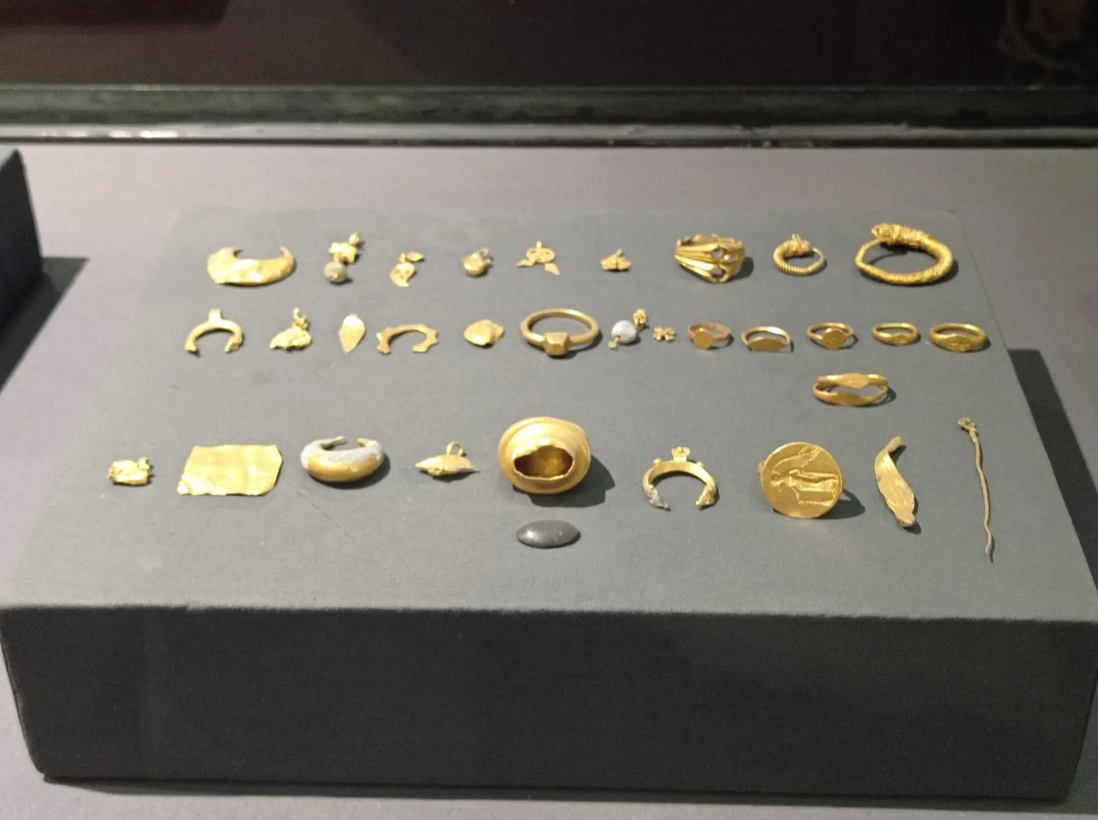 Peças de ouro expostas sobre uma base, incluindo anéis, pulseiras e outros adornos.