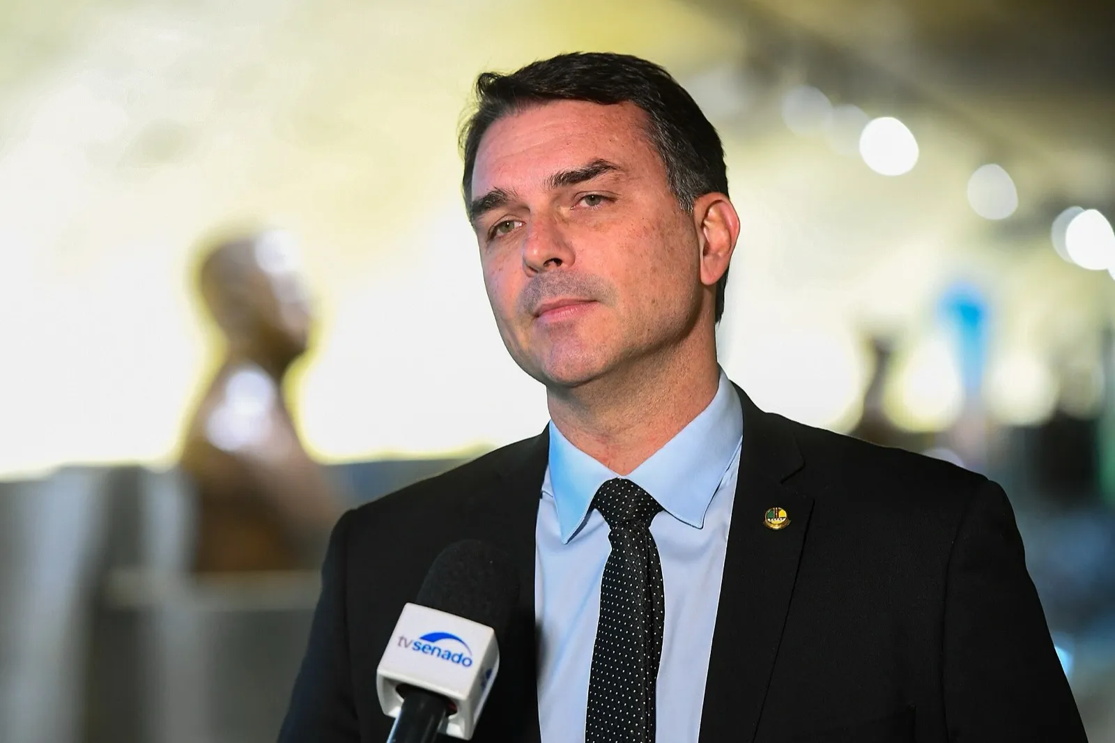 Flávio Bolsonaro, de terno escuro e gravata, fala ao microfone da TV Senado.
