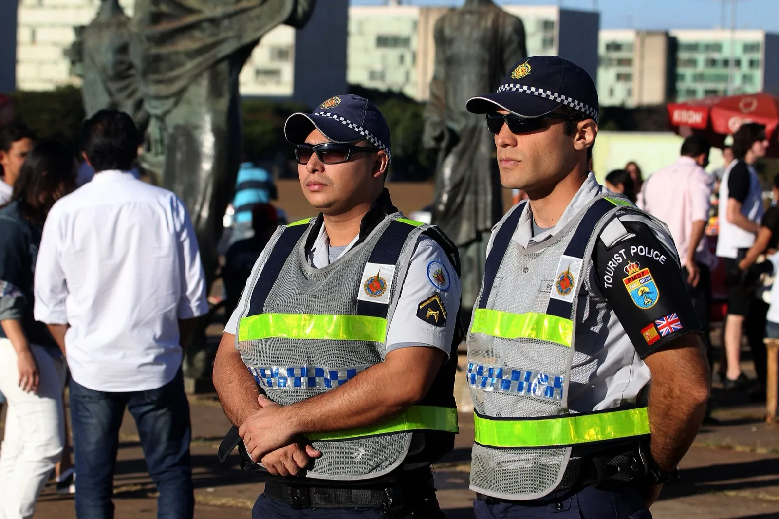 Dois policiais militares do Distrito Federal, de boné, óculos escuros e colete refletivo, em pé numa praça de Brasília.