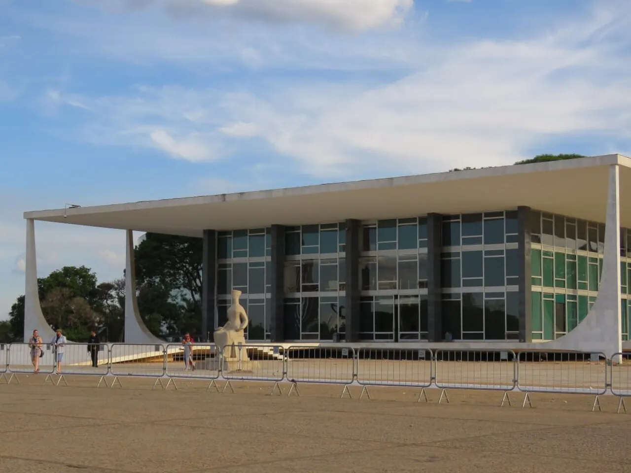 Fachada do Palácio do Supremo Tribunal Federal, com colunas brancas curvas e a estátua A Justiça à frente, atrás de grades na Praça dos Três Poderes.