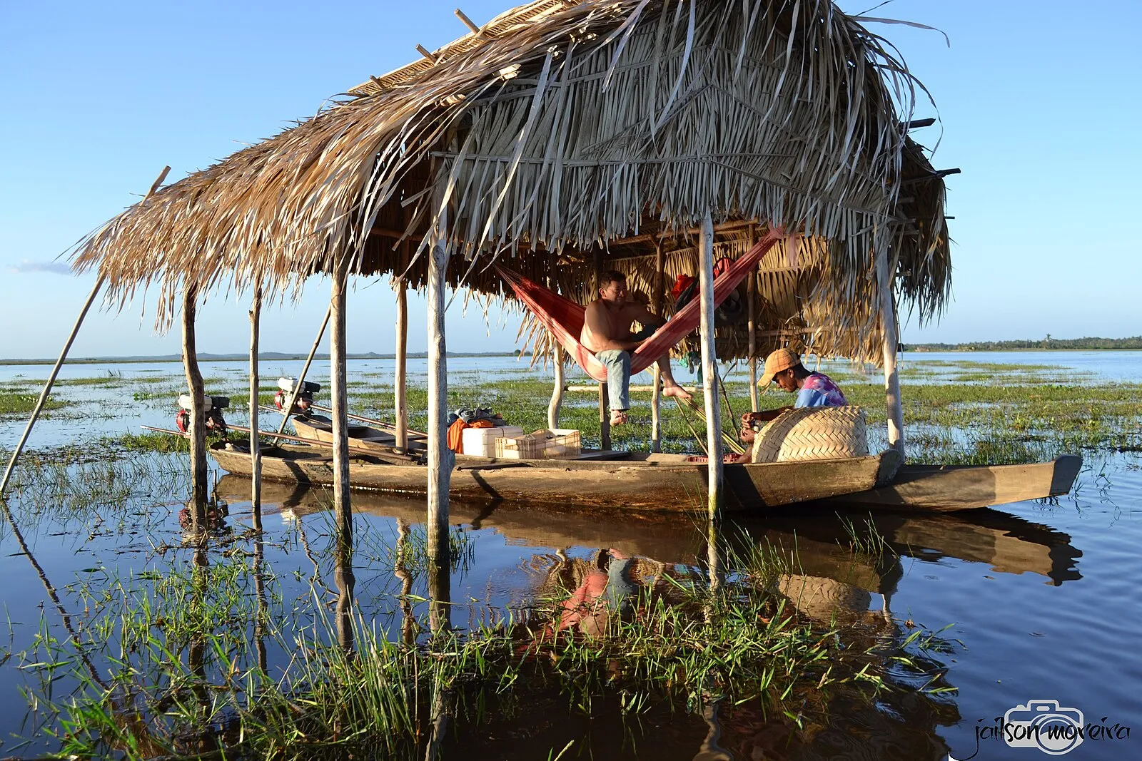 Pescadores em canoas junto a uma cabana de palha no rio Pericumã.