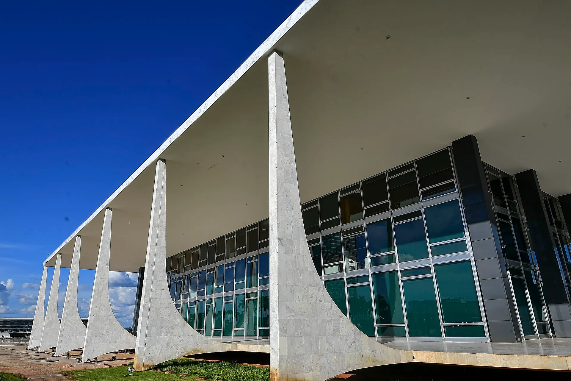 Fachada do prédio do Supremo Tribunal Federal, em Brasília, com colunas curvas de mármore, grandes janelas de vidro e céu azul.